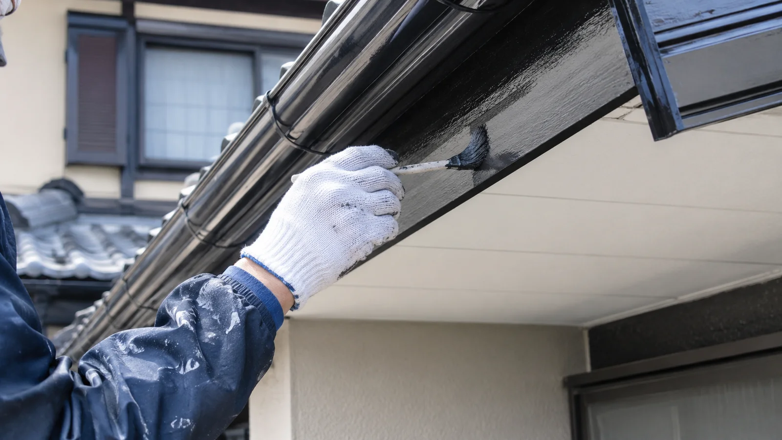 白い手袋をはめた職人が刷毛を使い、住宅の雨樋や破風板などの付帯部を丁寧に黒色で塗装している作業中の手元のクローズアップ写真

[ChatGPT image2] 雨樋・破風・軒天など付帯部を職人が刷毛で丁寧に塗装している手元のクローズアップ